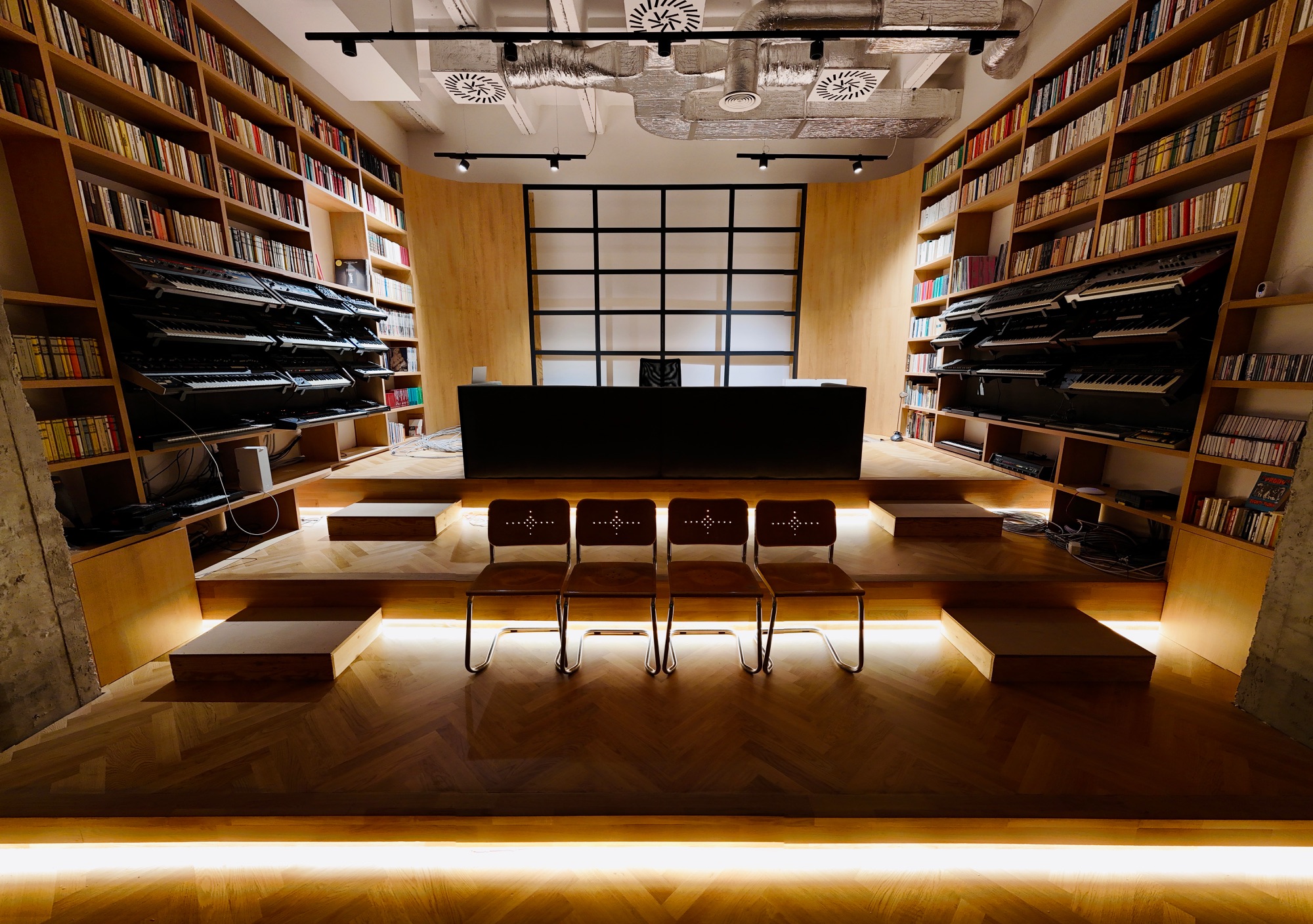 Interior of noiseburg studio — wooden shelves with books and synthesizers, stage with chairs.