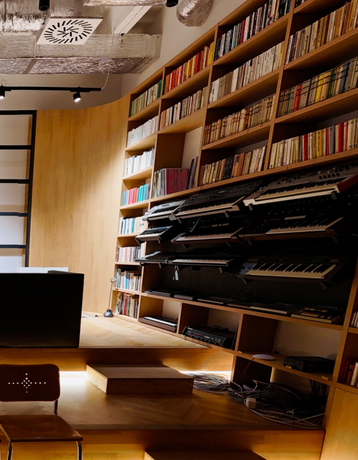 Close-up of a wall of synthesizers and a library.